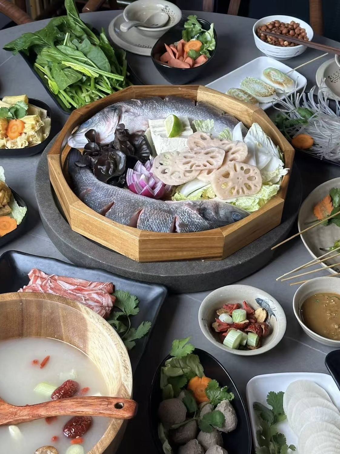 八角木盤上的整條鮮魚，配藕片、木耳、白菜與豆腐，桌上擺滿配菜