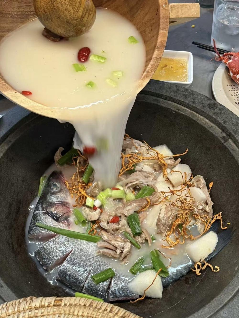 奶白魚湯從木盆倒入滾燙石鍋，鍋中有魚、羊肉片與蟲草花